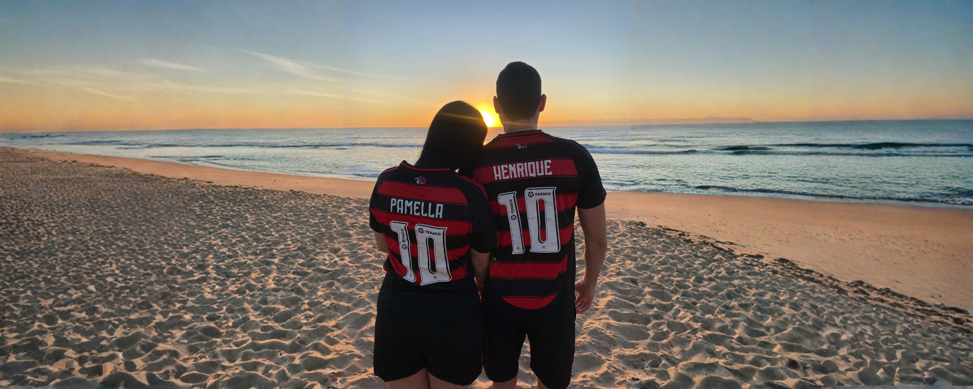 Pamella e Henrique na praia ao pôr do sol, vestindo as camisas do Flamengo